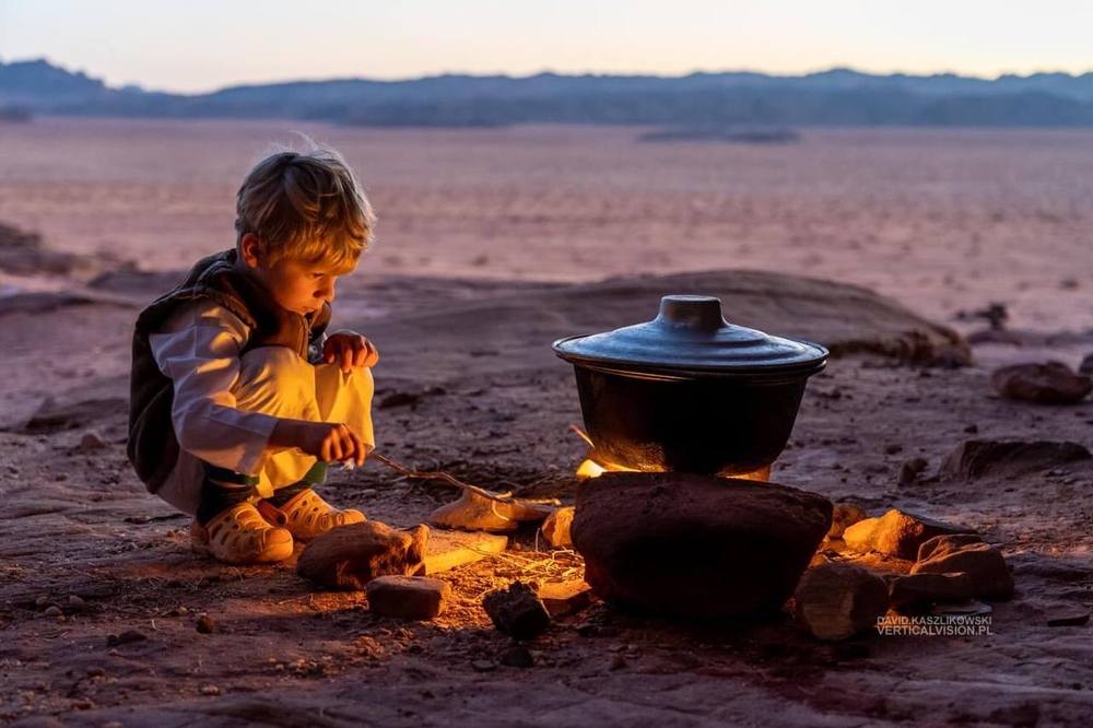 Young boy tending a fire next to a cooking pot at dusk